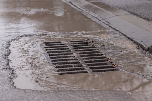 Stormwater flowing into a municipal street drain representing drainage operations and budget planning